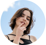 Profile photo of a young person wearing a black dress, standing against a background of the sky