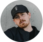Profile photo of a young person wearing a black hat and sweat shirt, standing in front of a concrete wall.